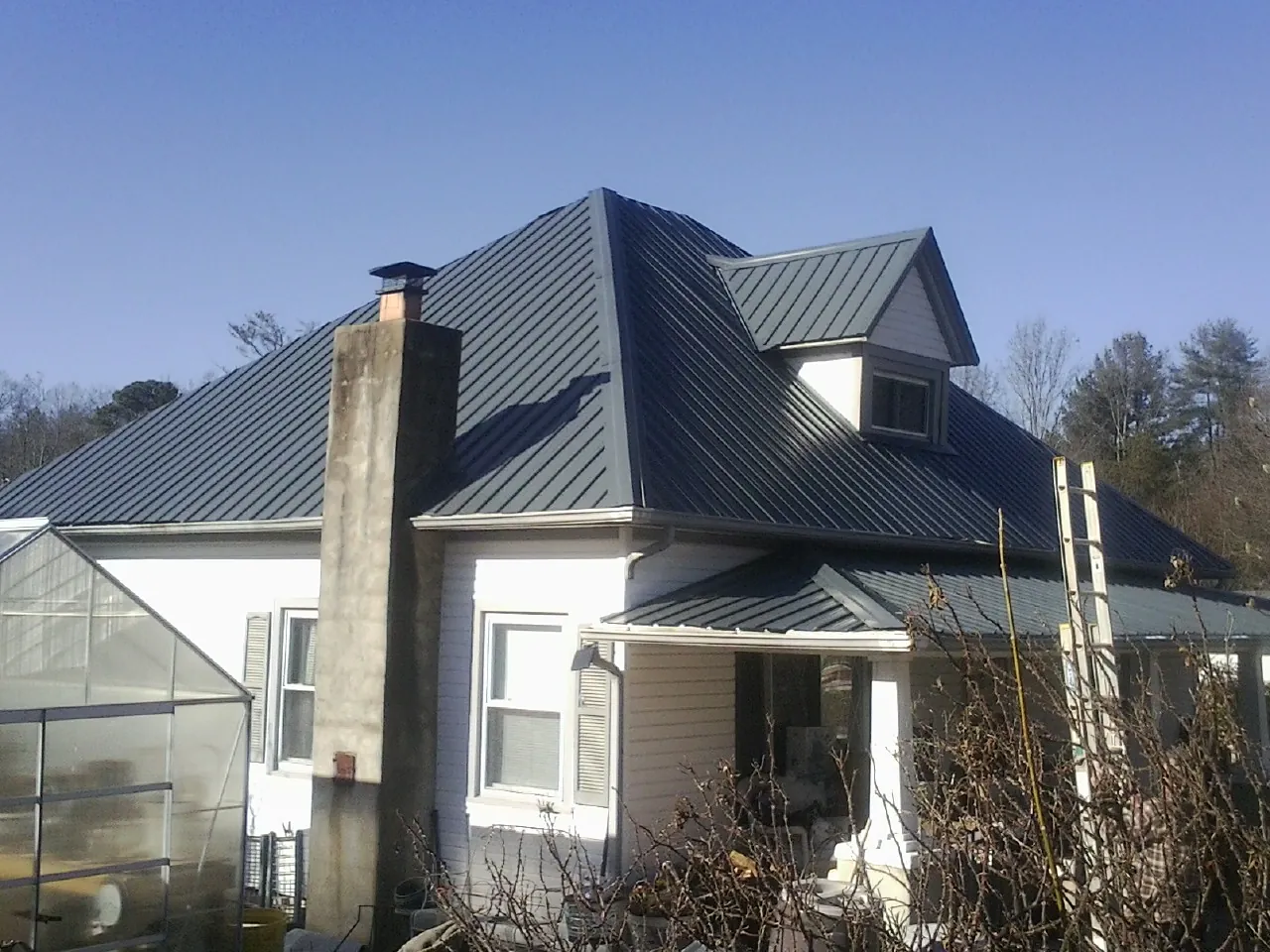 Dark blue standing seam metal roof on a white farmhouse with dormer — Slate & Tile Roof Repair by Roofing Brothers in Battleboro