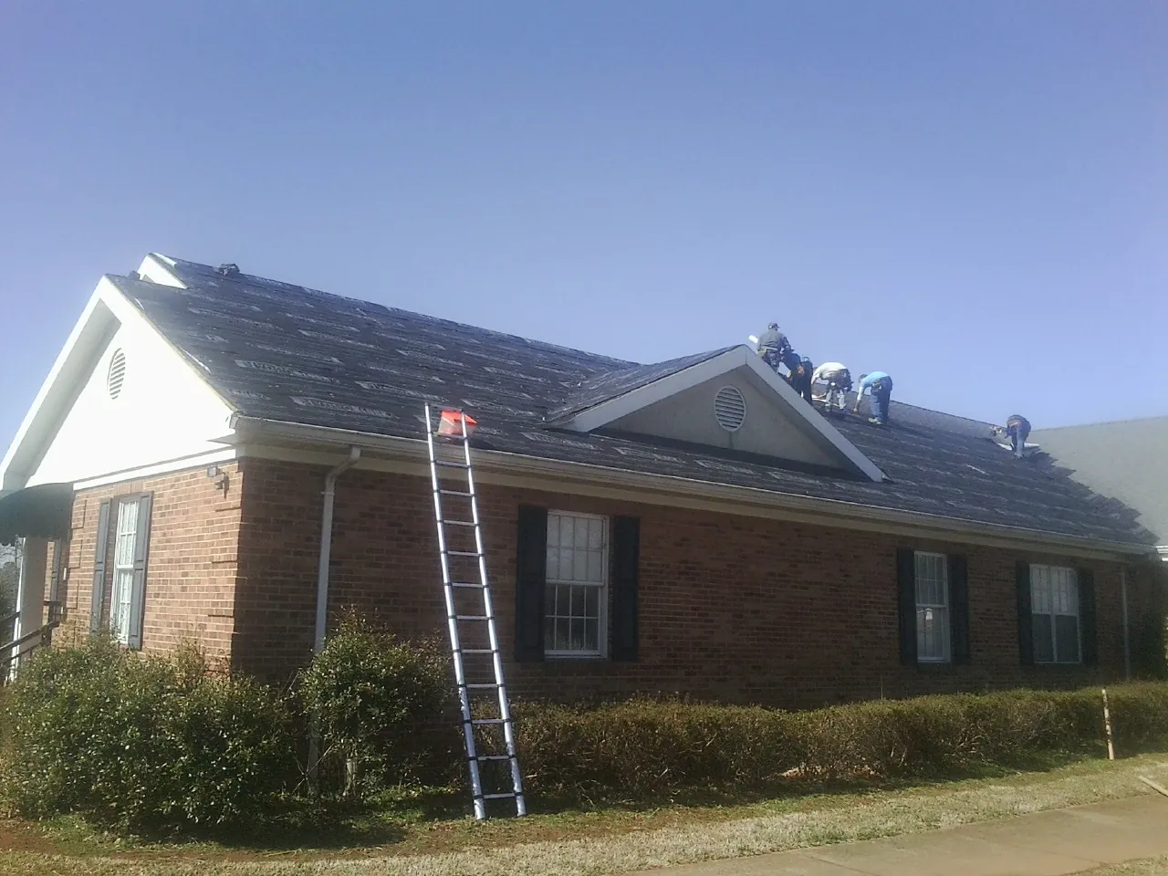 Crew tearing shingles off a brick ranch roof with a ladder set — Emergency Roof Repair work by our crew in Battleboro