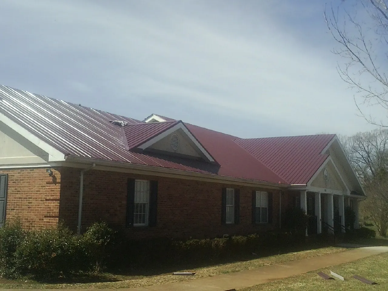 Red metal roof with gabled entries on a long brick building, from a Hail Damage Roof Repair job in Battleboro