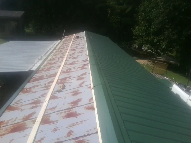 Old rusted panels beside newly installed green metal roofing — Wind Damage Roof Repair by Roofing Brothers in Battleboro