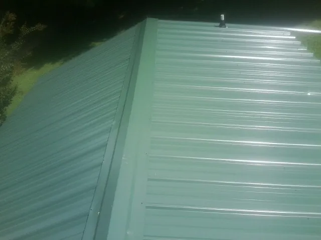 New green metal panels meeting at the ridge of a roof — Flat Roof Repair work by our crew in Battleboro