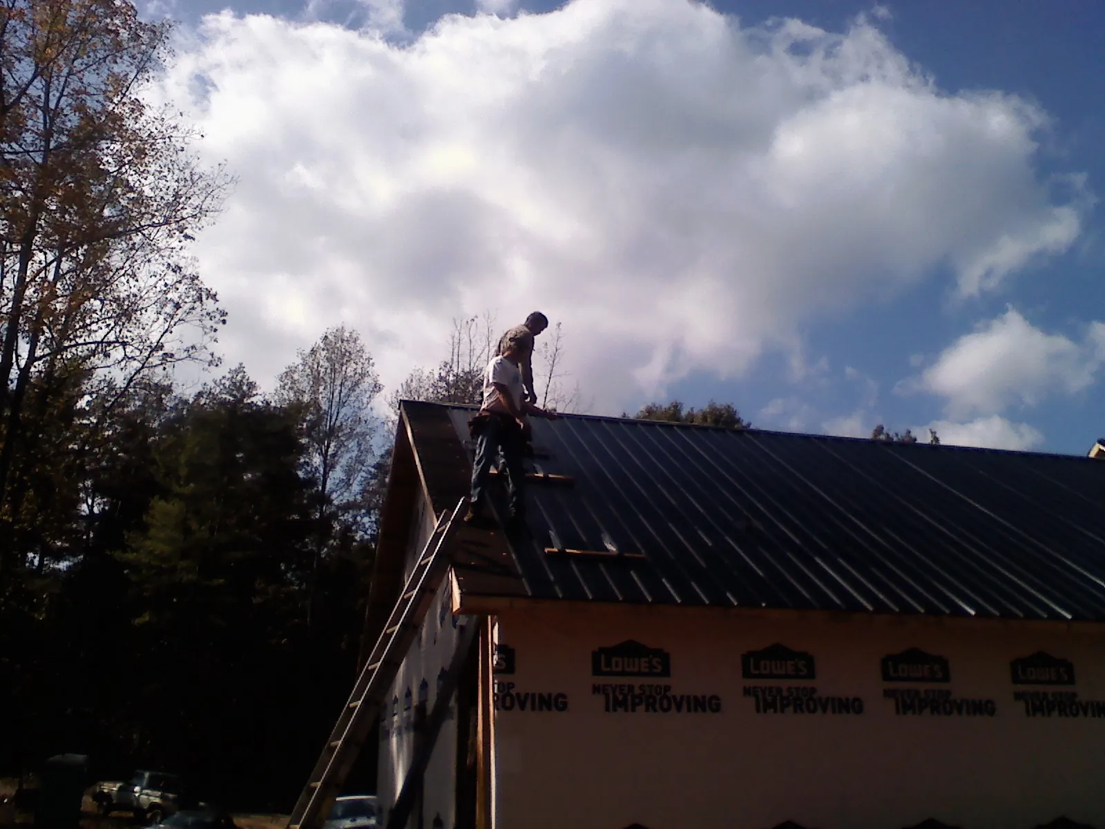 Roofer fastening dark metal panels high against a cloudy sky, from a Roof Inspection job in Battleboro