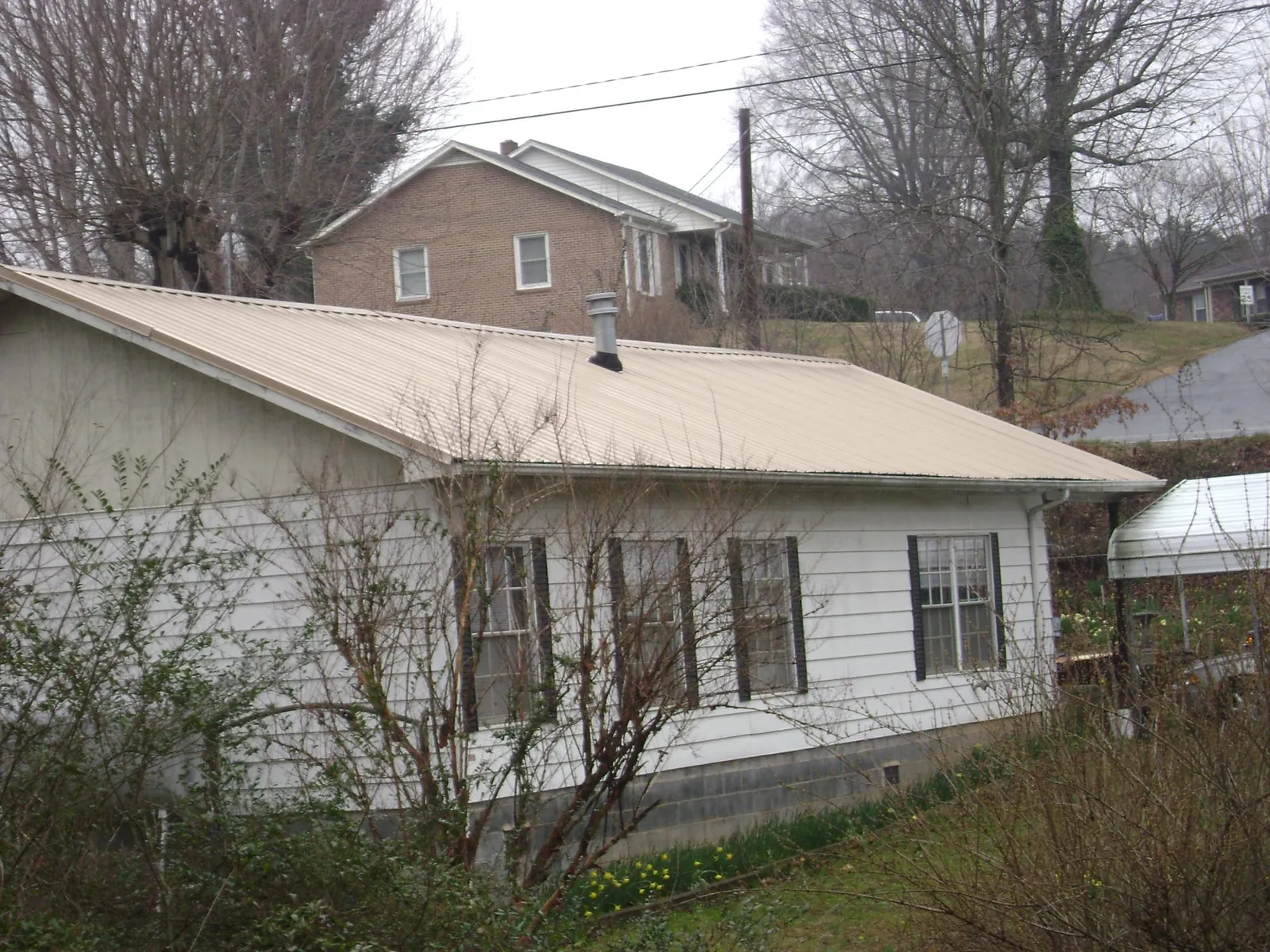Tan metal roof on a white sided house set into a hillside — Commercial Roofing by Roofing Brothers in Battleboro