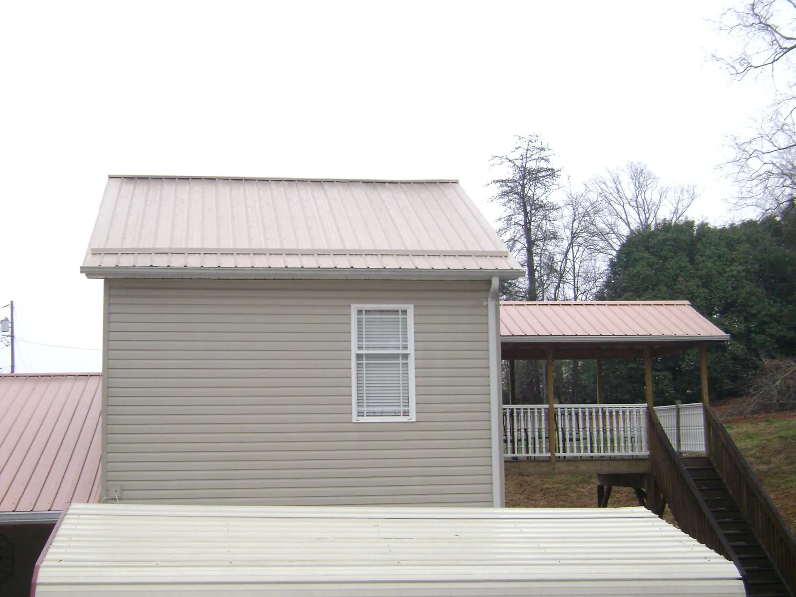 Tan metal roofs on a two story addition and attached porch, from a Roof Replacement job in Battleboro